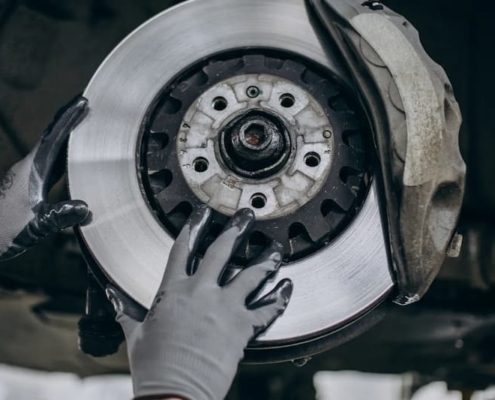 Mechanik w rękawicach sprawdza stan tarczy hamulcowej i zacisku podczas kontroli zużycia klocków hamulcowych