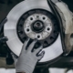 Mechanik w rękawicach sprawdza stan tarczy hamulcowej i zacisku podczas kontroli zużycia klocków hamulcowych